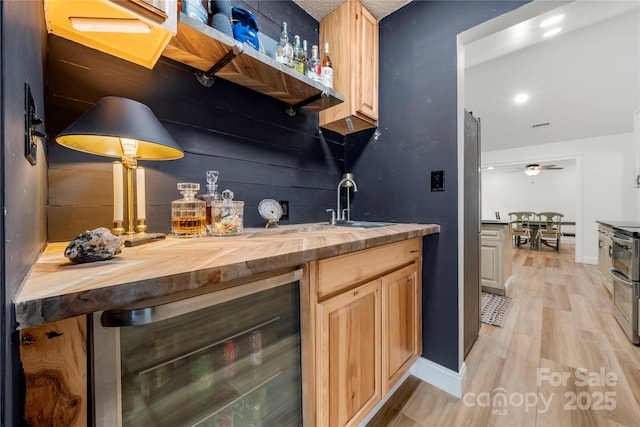 bar with wine cooler, light wood-style flooring, indoor wet bar, and baseboards