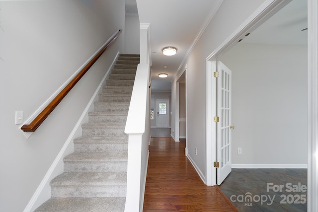 stairs with baseboards, wood finished floors, and ornamental molding