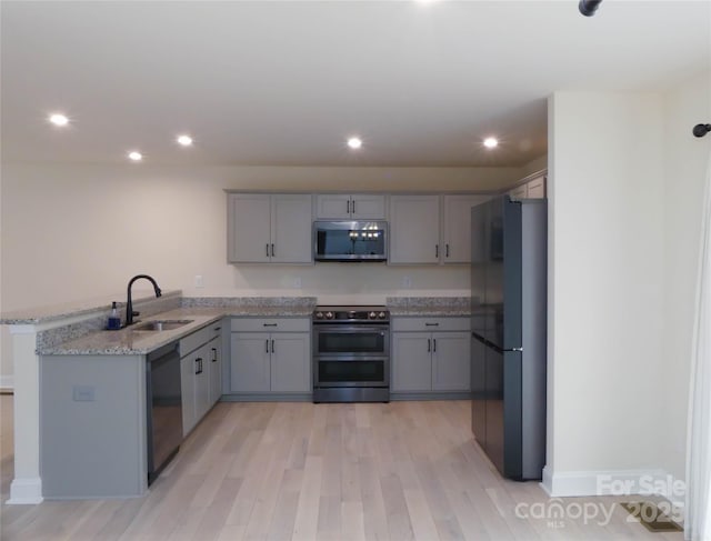 kitchen featuring recessed lighting, gray cabinets, a peninsula, stainless steel appliances, and a sink