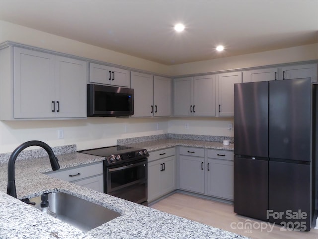 kitchen featuring gray cabinets, a sink, stainless steel microwave, range with electric stovetop, and freestanding refrigerator