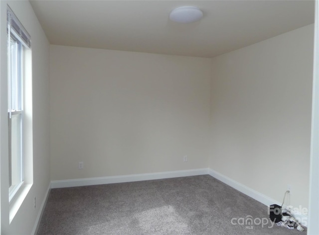 spare room featuring dark carpet and baseboards