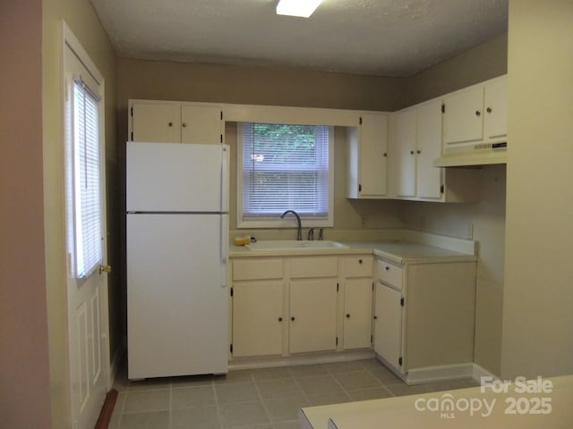 kitchen with a sink, under cabinet range hood, white cabinetry, freestanding refrigerator, and light countertops