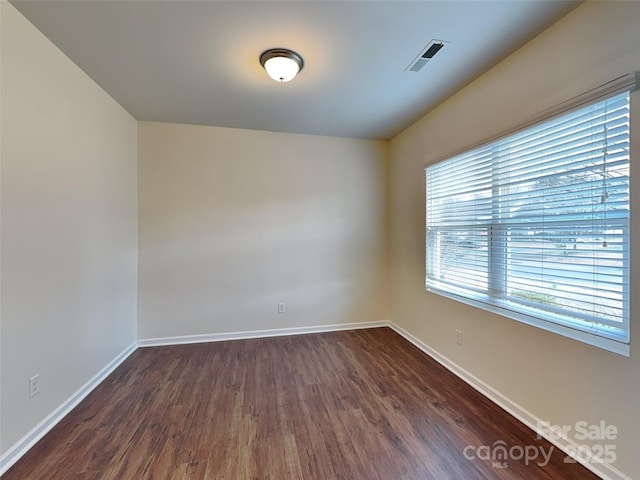 unfurnished room with dark wood finished floors, visible vents, and baseboards