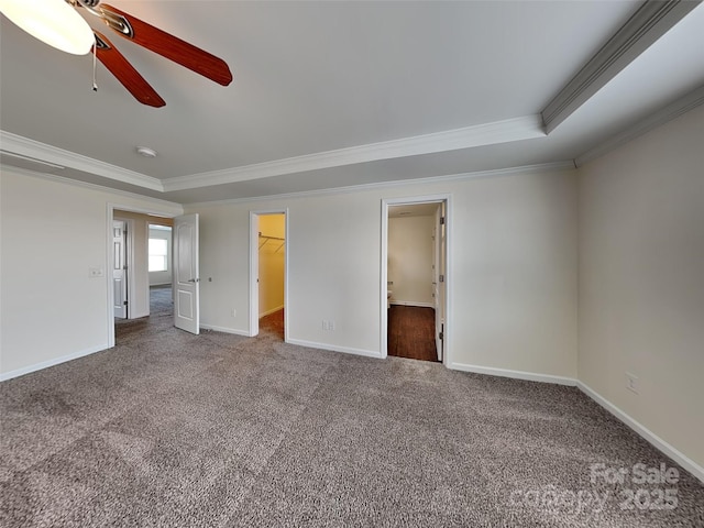 unfurnished bedroom with crown molding, baseboards, a walk in closet, a tray ceiling, and carpet floors