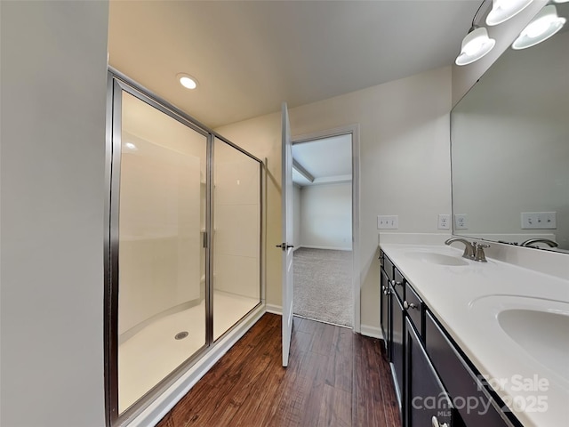 bathroom with wood finished floors, baseboards, double vanity, a sink, and a shower stall