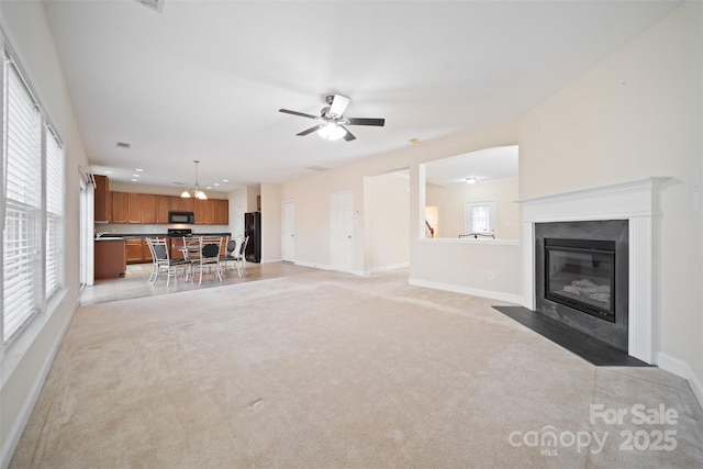 unfurnished living room with light carpet, a fireplace with flush hearth, ceiling fan, and baseboards