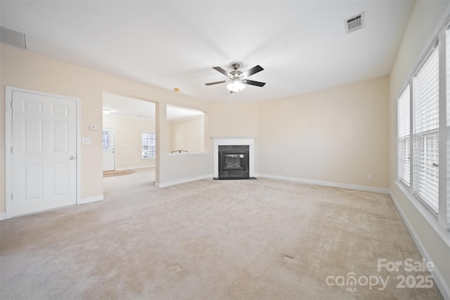 unfurnished living room with a ceiling fan, a fireplace with flush hearth, light colored carpet, and visible vents