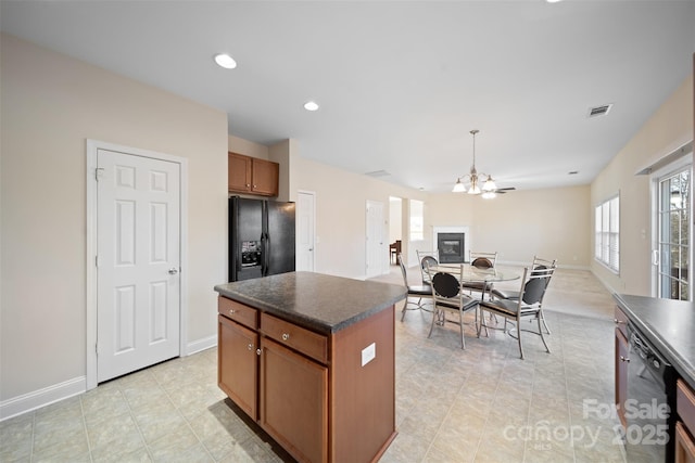 kitchen featuring black appliances, dark countertops, a center island, brown cabinetry, and a chandelier