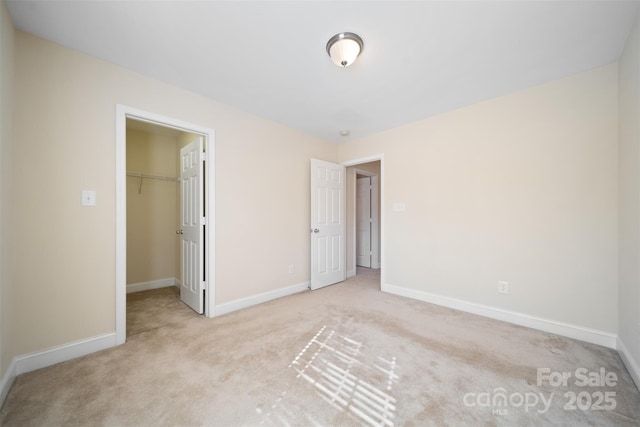 unfurnished bedroom with a spacious closet, baseboards, a closet, and light carpet