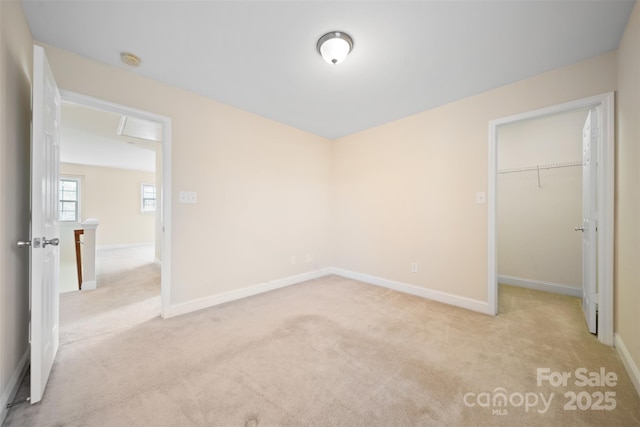 unfurnished bedroom with a closet, baseboards, light colored carpet, and a spacious closet