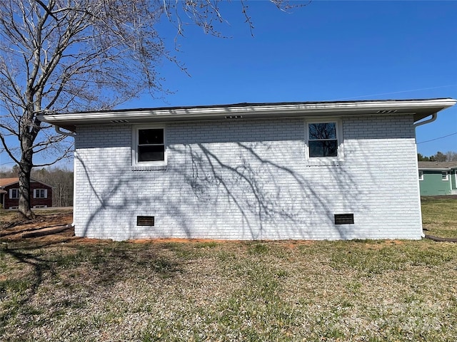 view of side of property with crawl space, brick siding, and a yard