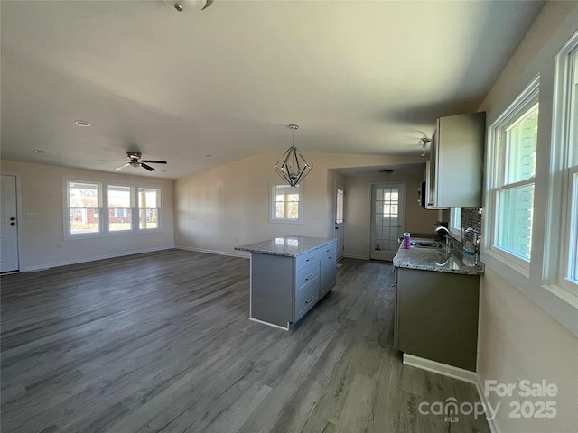 kitchen featuring a kitchen island, baseboards, ceiling fan, wood finished floors, and a sink