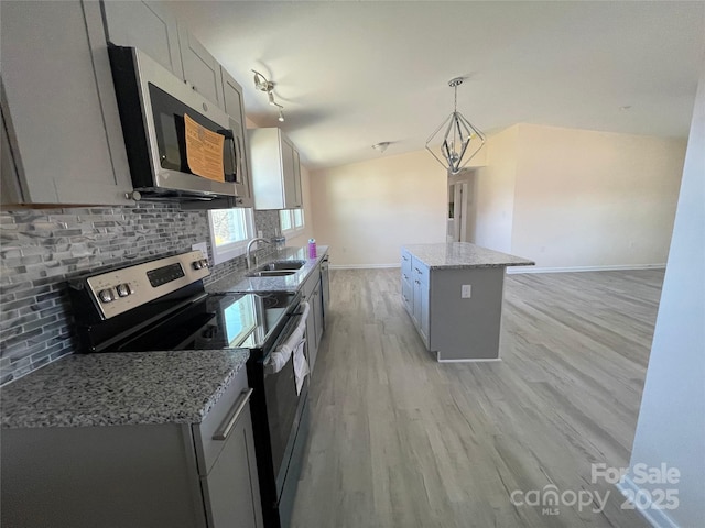 kitchen featuring lofted ceiling, a sink, decorative backsplash, stainless steel appliances, and light wood-type flooring