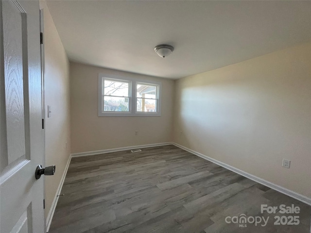 spare room featuring dark wood-type flooring and baseboards