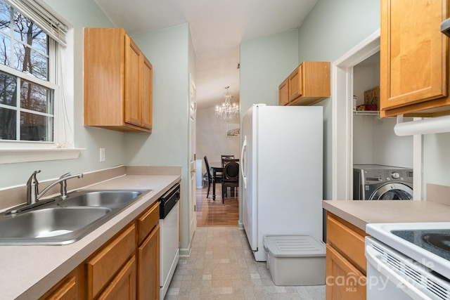 kitchen featuring white appliances, washer / clothes dryer, a sink, light countertops, and a notable chandelier