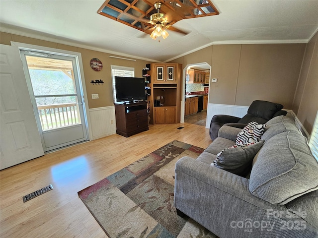 living room featuring wood finished floors, a wainscoted wall, visible vents, lofted ceiling, and arched walkways