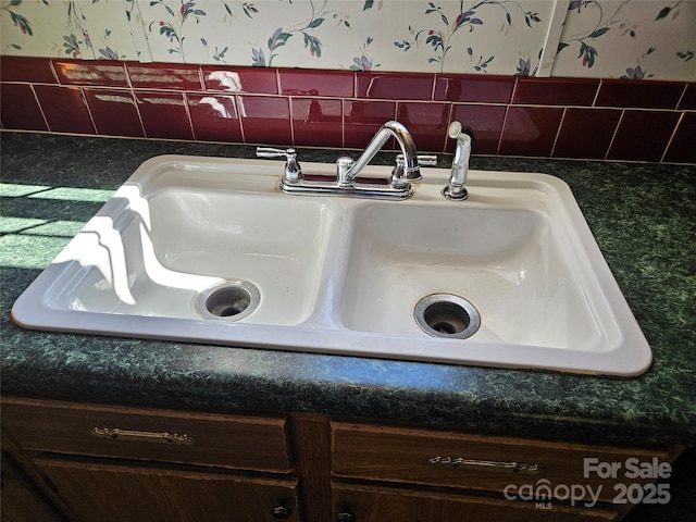 interior details featuring a sink, dark countertops, and wallpapered walls