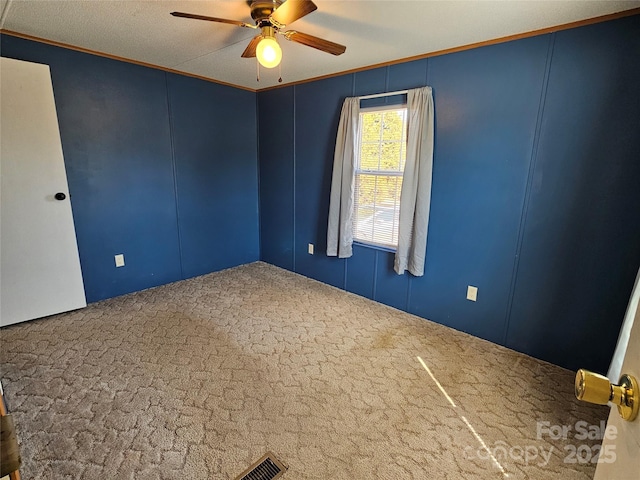 carpeted empty room featuring a decorative wall, a ceiling fan, and ornamental molding