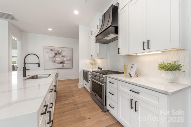 2021 S St, Charlotte, NC 28208 - kitchen featuring stainless steel appliances, custom exhaust hood, a sink, light wood-style flooring, and light stone countertops