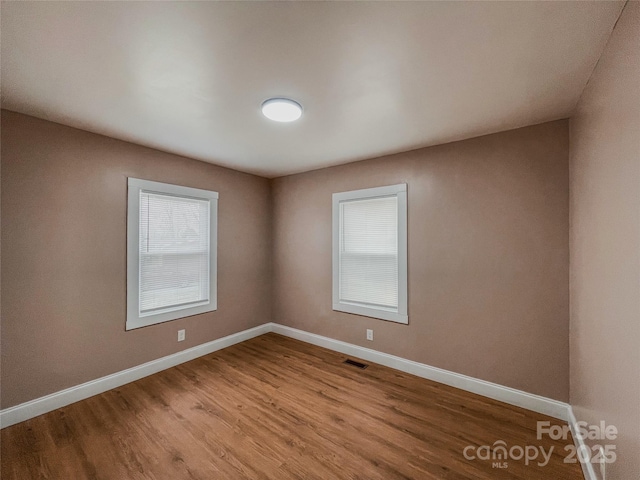 unfurnished room featuring visible vents, wood finished floors, and baseboards