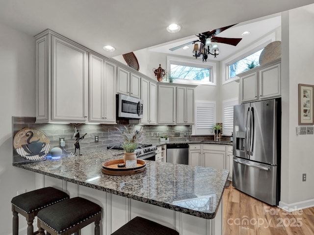 kitchen with dark stone countertops, a peninsula, a sink, appliances with stainless steel finishes, and backsplash