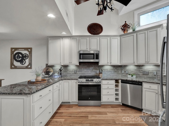 kitchen with a peninsula, light wood-style flooring, tasteful backsplash, and appliances with stainless steel finishes