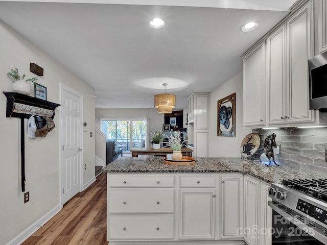 kitchen featuring backsplash, a peninsula, light wood-style floors, stone countertops, and stainless steel appliances