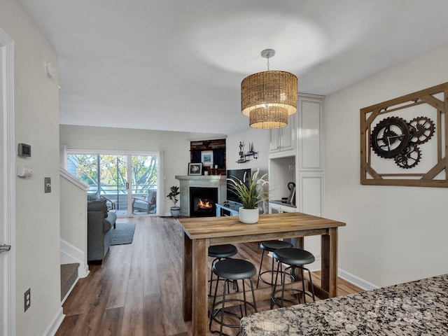 kitchen with a notable chandelier, wood finished floors, baseboards, and a lit fireplace