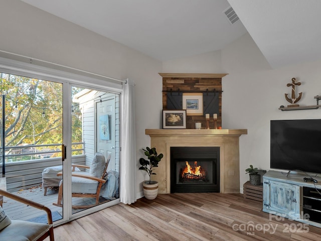 living room with visible vents, a warm lit fireplace, wood finished floors, and vaulted ceiling