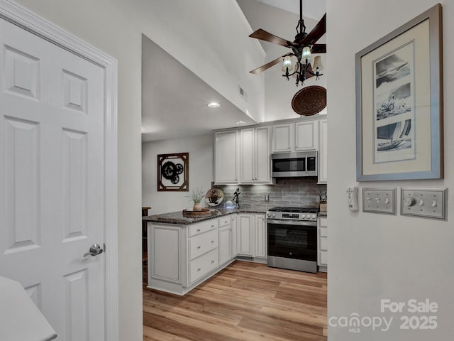 kitchen with dark stone countertops, white cabinetry, stainless steel appliances, and ceiling fan