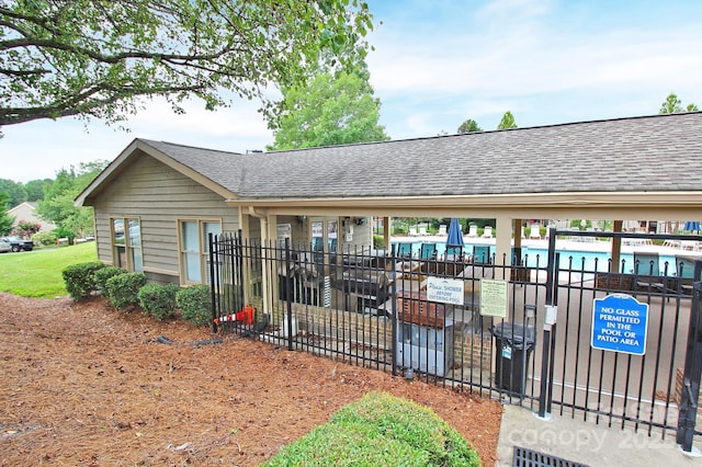 exterior space featuring a community pool, roof with shingles, and fence