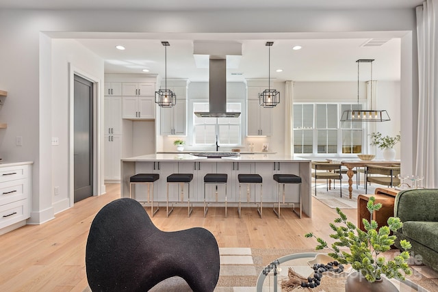 kitchen with a kitchen bar, white cabinetry, island range hood, light wood finished floors, and light countertops
