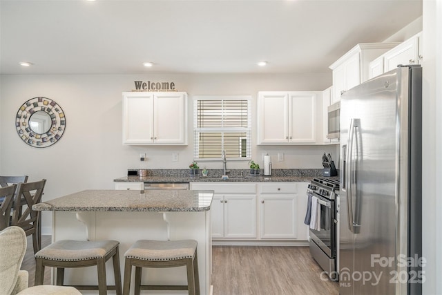 kitchen with light wood-type flooring, a sink, appliances with stainless steel finishes, a breakfast bar area, and white cabinets