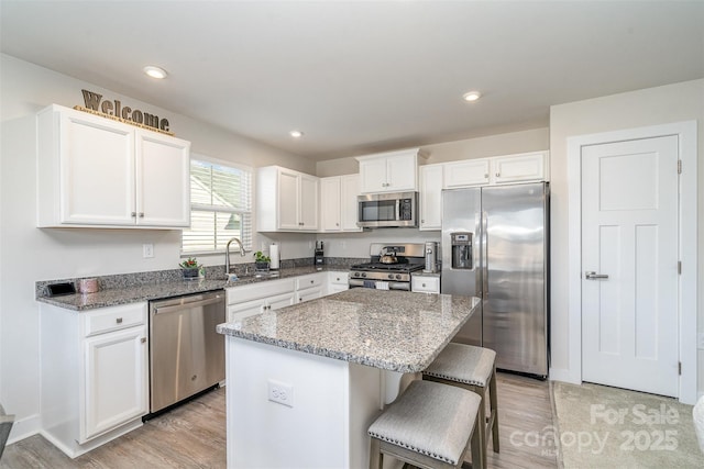 kitchen featuring light wood finished floors, a center island, stainless steel appliances, white cabinetry, and a sink