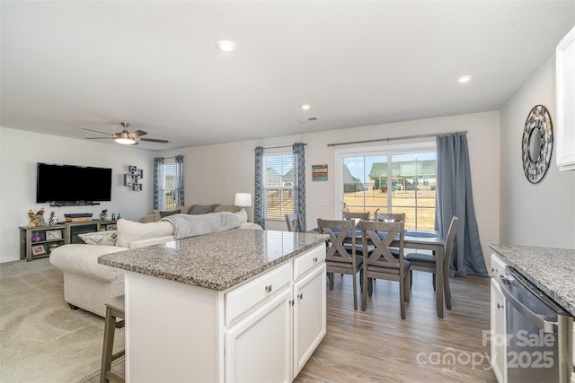 kitchen with a breakfast bar, light stone counters, white cabinets, a ceiling fan, and stainless steel dishwasher