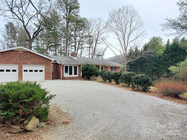 single story home with an attached garage, brick siding, driveway, and a chimney