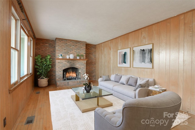 living area featuring wooden walls, a brick fireplace, visible vents, and wood-type flooring