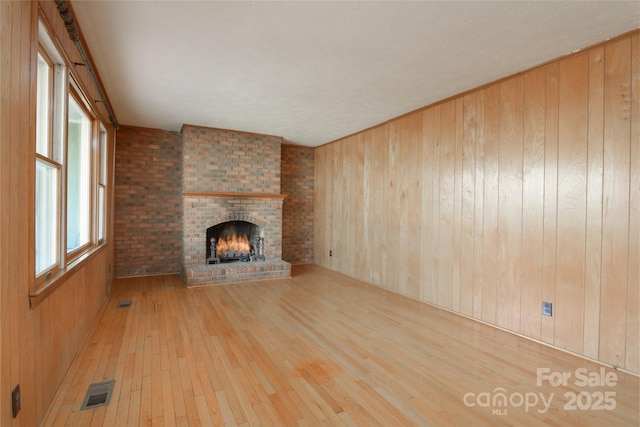 unfurnished living room with visible vents, wood walls, a fireplace, and hardwood / wood-style flooring