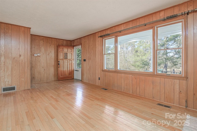 empty room featuring visible vents, wooden walls, and hardwood / wood-style floors