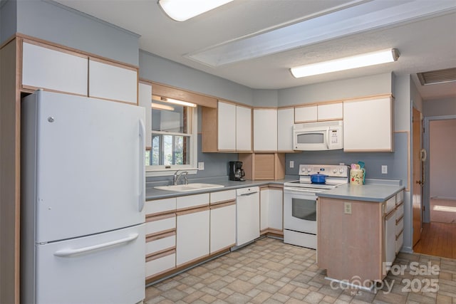 kitchen with a sink, white appliances, white cabinets, and light countertops