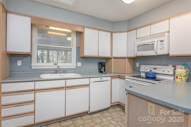 kitchen with a sink, stone finish flooring, white appliances, white cabinets, and light countertops