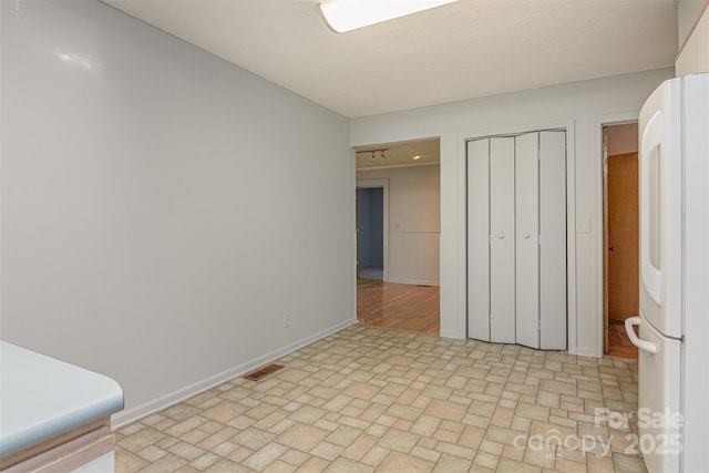 unfurnished bedroom with visible vents, a closet, freestanding refrigerator, and baseboards