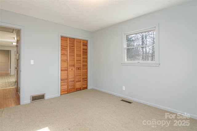 unfurnished bedroom with visible vents, carpet, attic access, and a closet