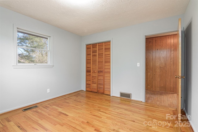 unfurnished bedroom with wood finished floors, visible vents, a closet, and a textured ceiling