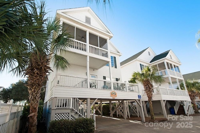 back of property featuring fence, stairway, concrete driveway, a sunroom, and a carport