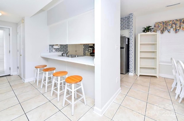 kitchen featuring visible vents, a breakfast bar, freestanding refrigerator, light countertops, and light tile patterned floors