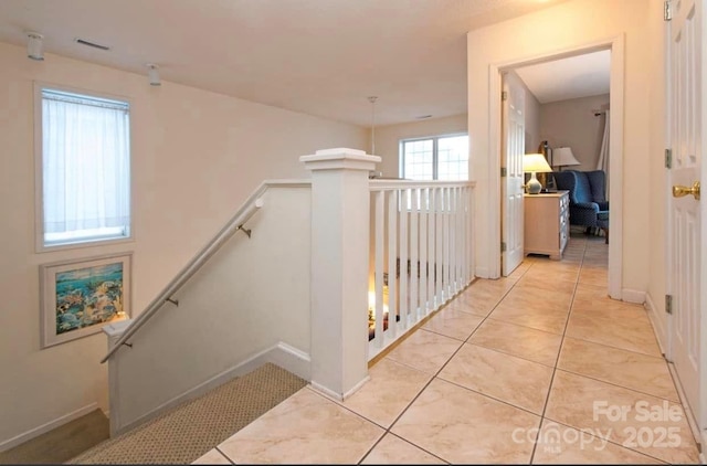 hall featuring light tile patterned floors, baseboards, and an upstairs landing