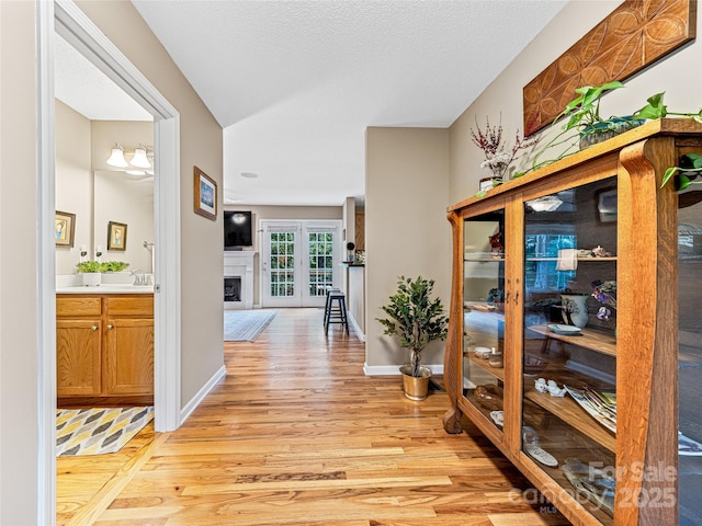 corridor with light wood finished floors, a textured ceiling, and baseboards