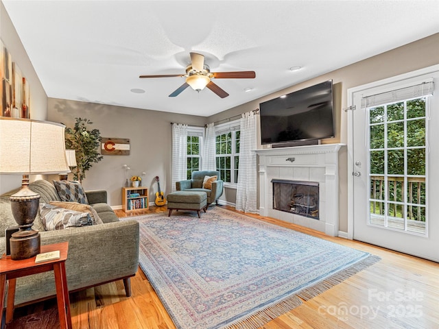 living area with baseboards, wood finished floors, a ceiling fan, and a tile fireplace