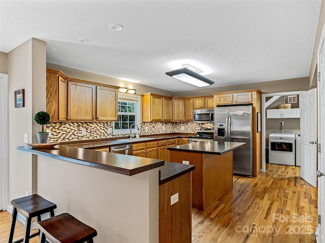 kitchen featuring dark countertops, a breakfast bar area, light wood-type flooring, stainless steel appliances, and washer / clothes dryer